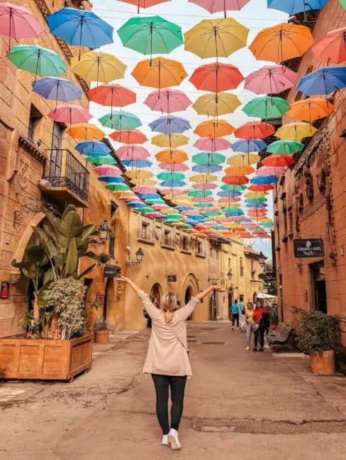 Poble Espanyol, Barcelona. Co videt v Barceloně. Dívka stojící na ulici, nad hlavou barevné deštníky